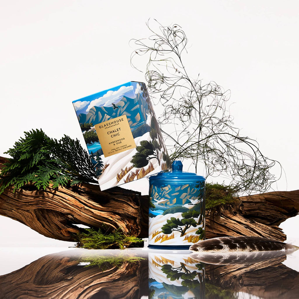 Blue candle with nature-themed design on a reflective surface with decorative elements.