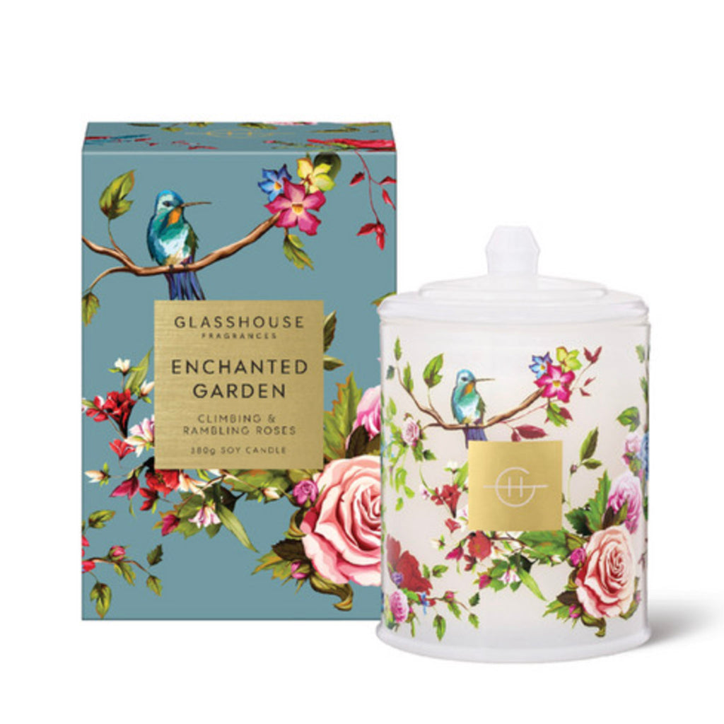 Glasshouse Fragrances Enchanted Garden 13.4 ounce floral scented soy wax candle in milky glass vessel with floral print and glass lid beside a blue floral gift box, front view.
