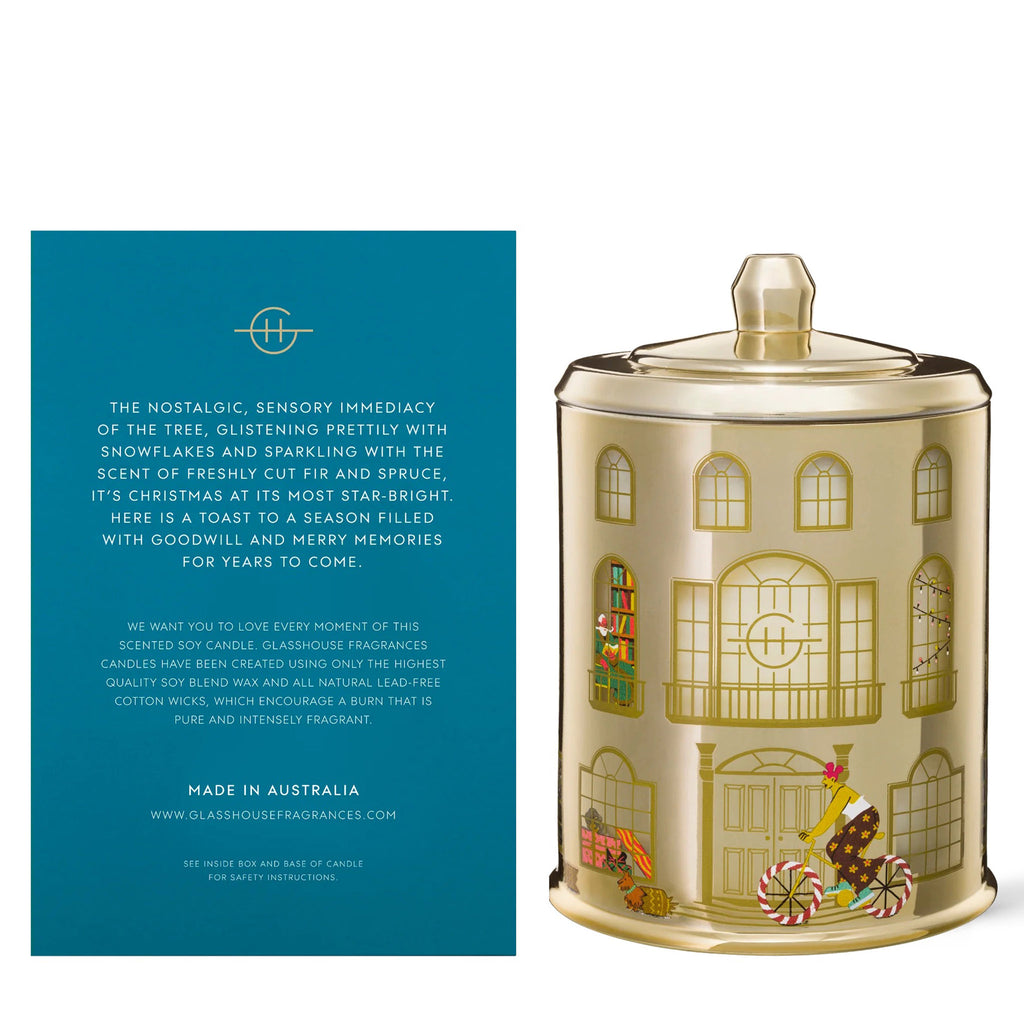 Glasshouse Fragrances Winter Wonderland 26.8 ounce frosted fir and snow gum scented soy wax candle in house illustrated gold glass jar with lid beside a blue and pink house gift box, rear view.