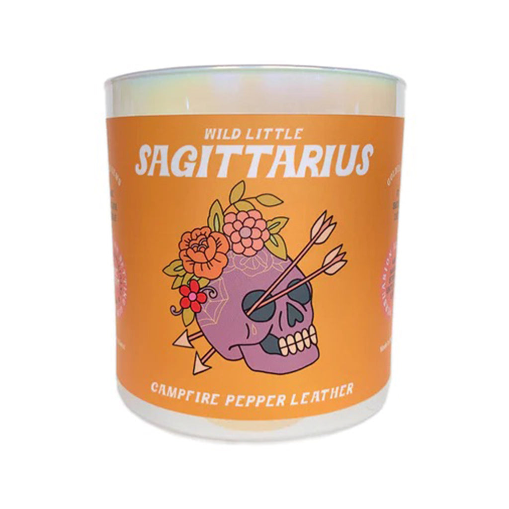 Golden Gems Wild Little Sagittarius Campfire and Pepper Leather scented soy wax candle with illustrated orange label on an iridescent white glass tumbler, front view.