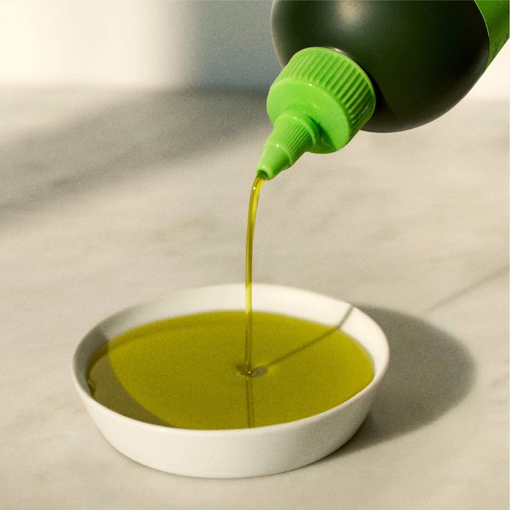 Graza "Drizzle" Extra Virgin Olive Oil in dark green squeeze bottle with oil being poured out into a small white dish to see color.