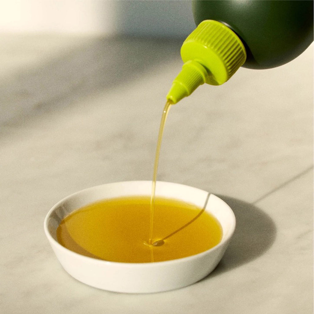 Graza "Sizzle" Extra Virgin Olive Oil in dark green squeeze bottle with oil being poured out into a small white dish to see color.