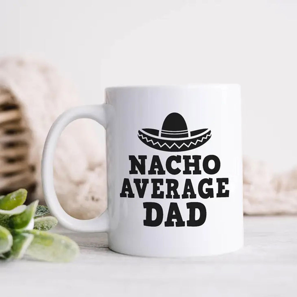 Heart & Willow Prints 11 ounce white ceramic mug with "Nacho Average Dad" and a sombrero illustration in black, handle is on the left.