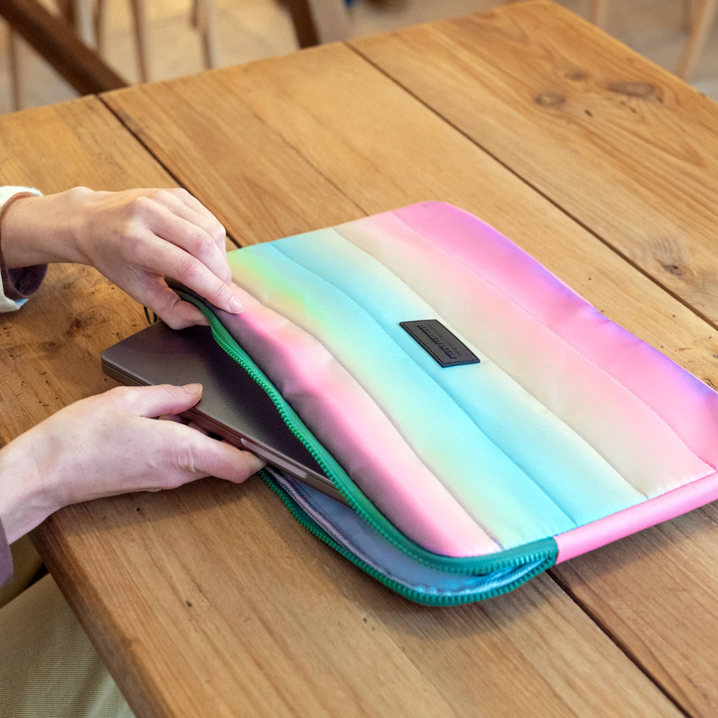 Person placing a laptop into a pastel gradient case on a wooden table.