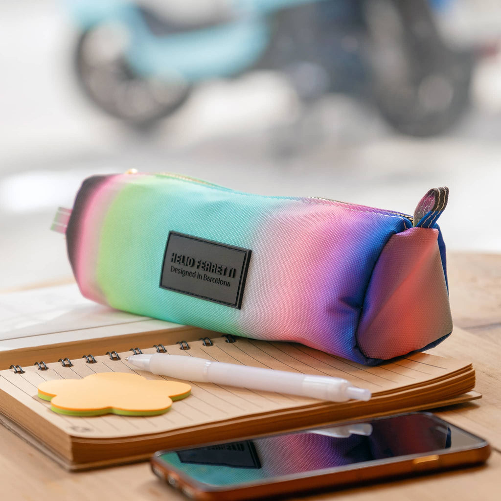 Pastel gradient pencil case on a notebook with stationery items on a blurred background.