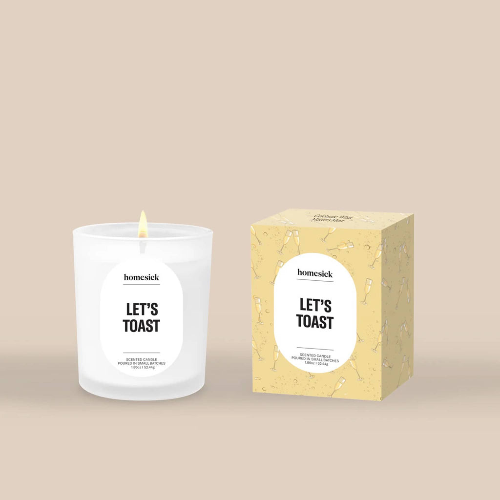 Homesick 'Let's Toast' mini candle and illustrated pale yellow packaging on a beige background.