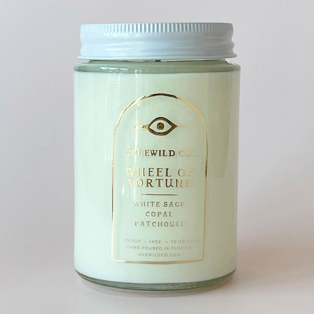 Idlewild Co. x Botanica Candle Wheel of Fortune Tarot Candle with scented soy wax in clear glass jar with white aluminum lid, back view with scent notes and info in gold foil.