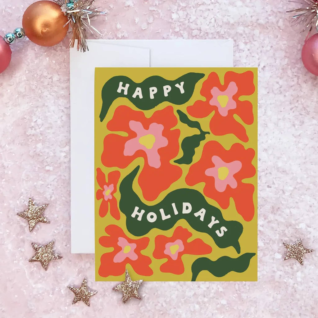 Floral card with 'Happy Holidays' text on a pink textured background with Christmas decorations.