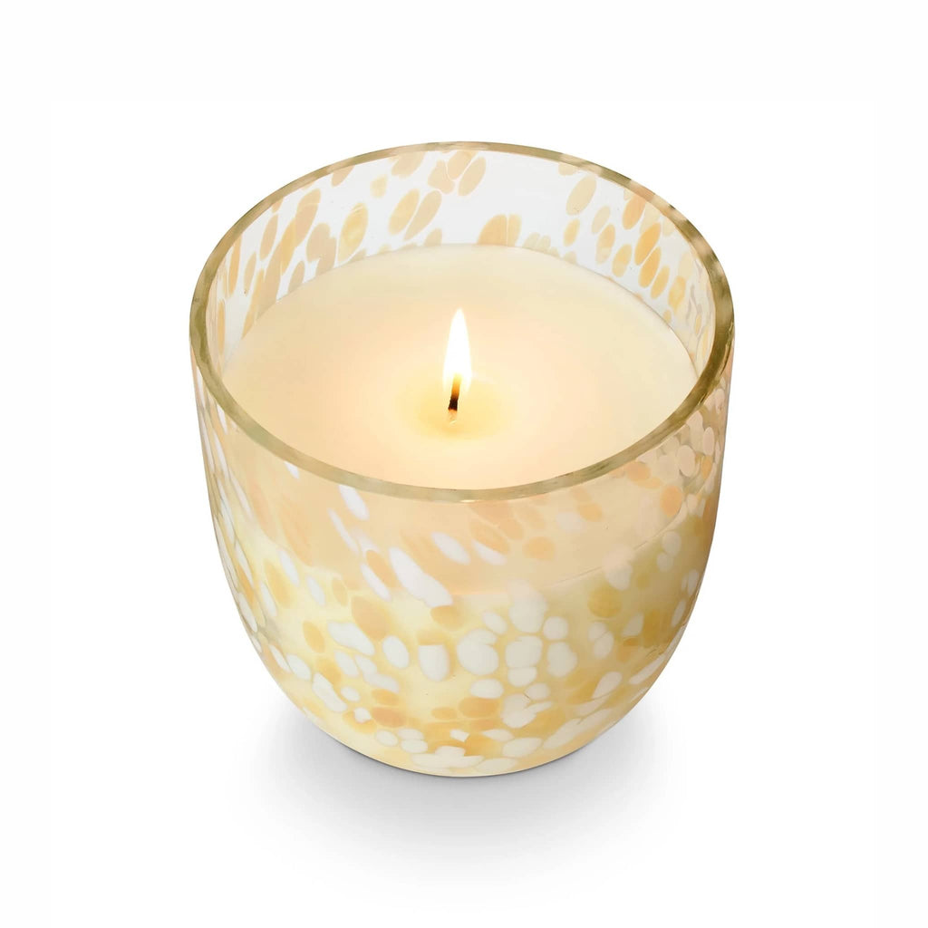 Illume Aperol Crush scented soy wax candle in orange and white speckled sun glass vessel, overhead view, wick lit.