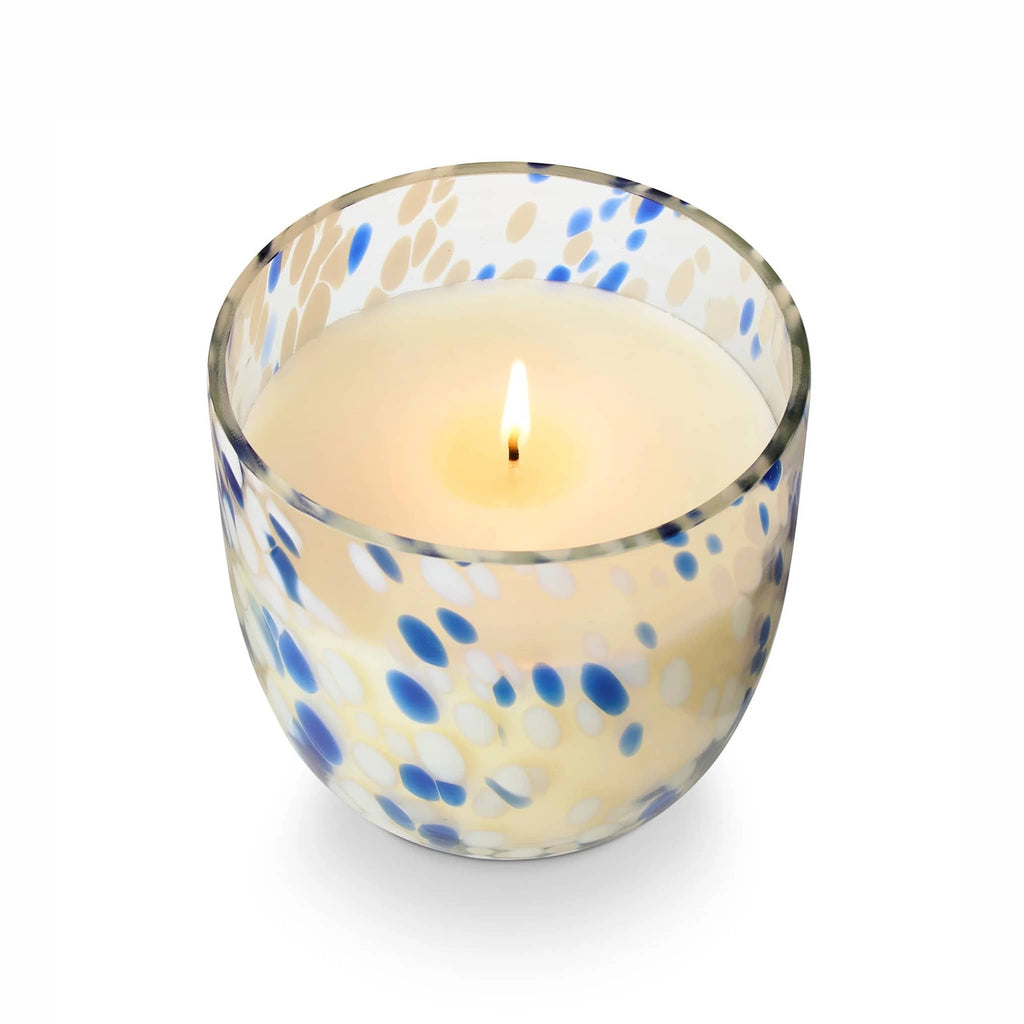 Illume Beach Towel scented soy wax candle in blue and white speckled sun glass vessel, overhead view, wick lit.