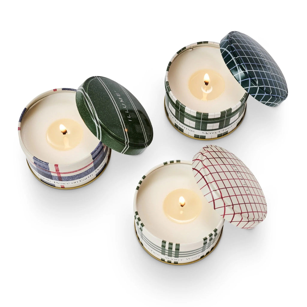 Illume Balsam and Cedar Scented Holiday Candle Mini Tin Trio Gift Set, each tin with lid has a different plaid pattern in green, red and blue. All lids are resting against the side of the tin and wicks are lit.