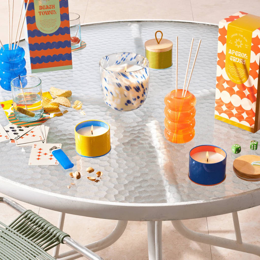 Illume Under the Sun Summer scent collection on a patio table with props.