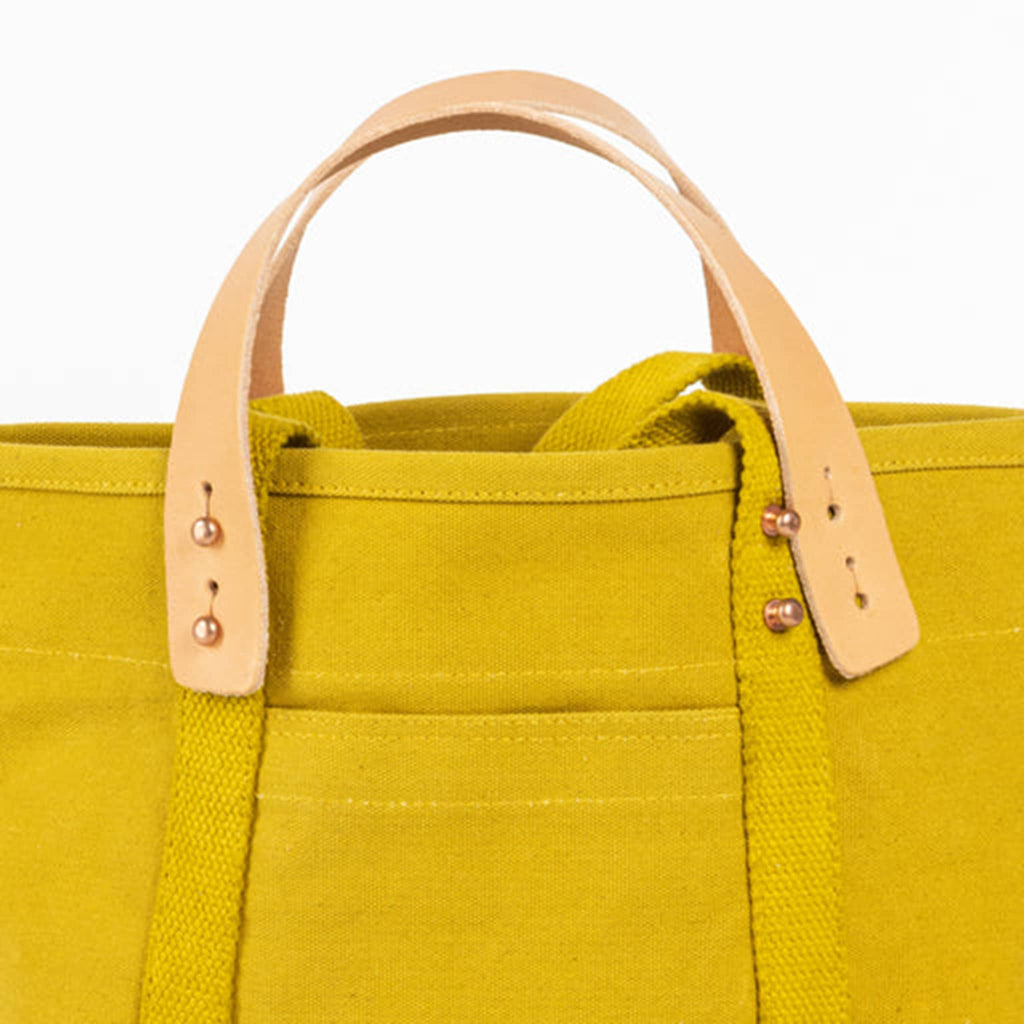 Chartreuse canvas tote bag, detail of removable leather handles, front view, on a white background.