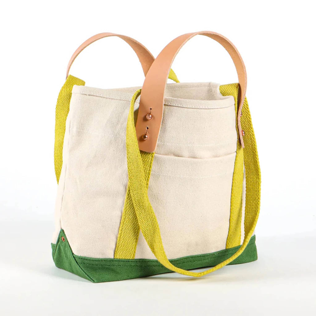 Natural canvas tote bag with green base and chartreuse straps with removable leather handles, front angle view, on a white background.