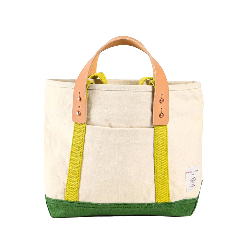 Natural canvas tote bag with green base and chartreuse straps with removable leather handles, front view, on a white background.