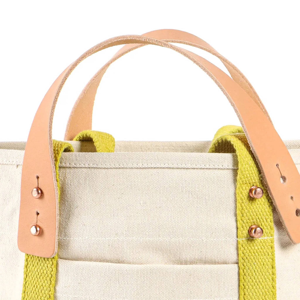 Natural canvas tote bag with green base and chartreuse straps, detail of removable leather handles on a white background.
