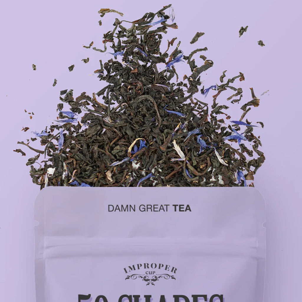 Improper Cup 50 Shades of Earl Grey black tea with caffeine in purple illustrated resealable pouch on a matching purple background with a spill of tea leaves coming out of the top of the bag.