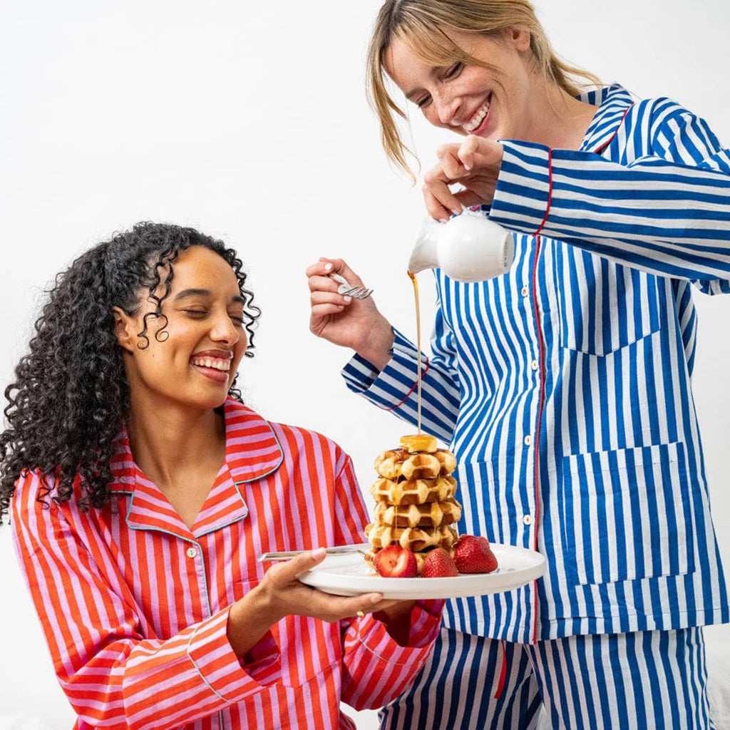 Two people in striped pajamas enjoying waffles with syrup and fruit.