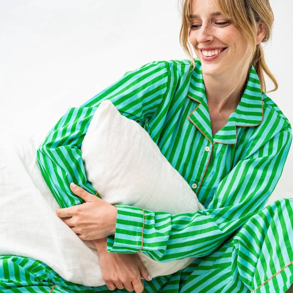 Woman wearing green and blue striped pajamas holding a white pillow.