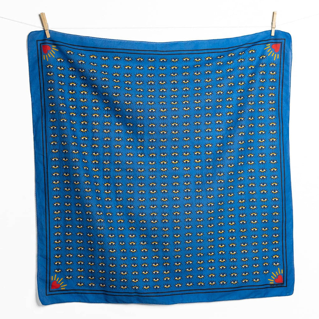 Blue scarf with eye pattern and hearts in the corner, hanging on a line with clothespins, on a white background.