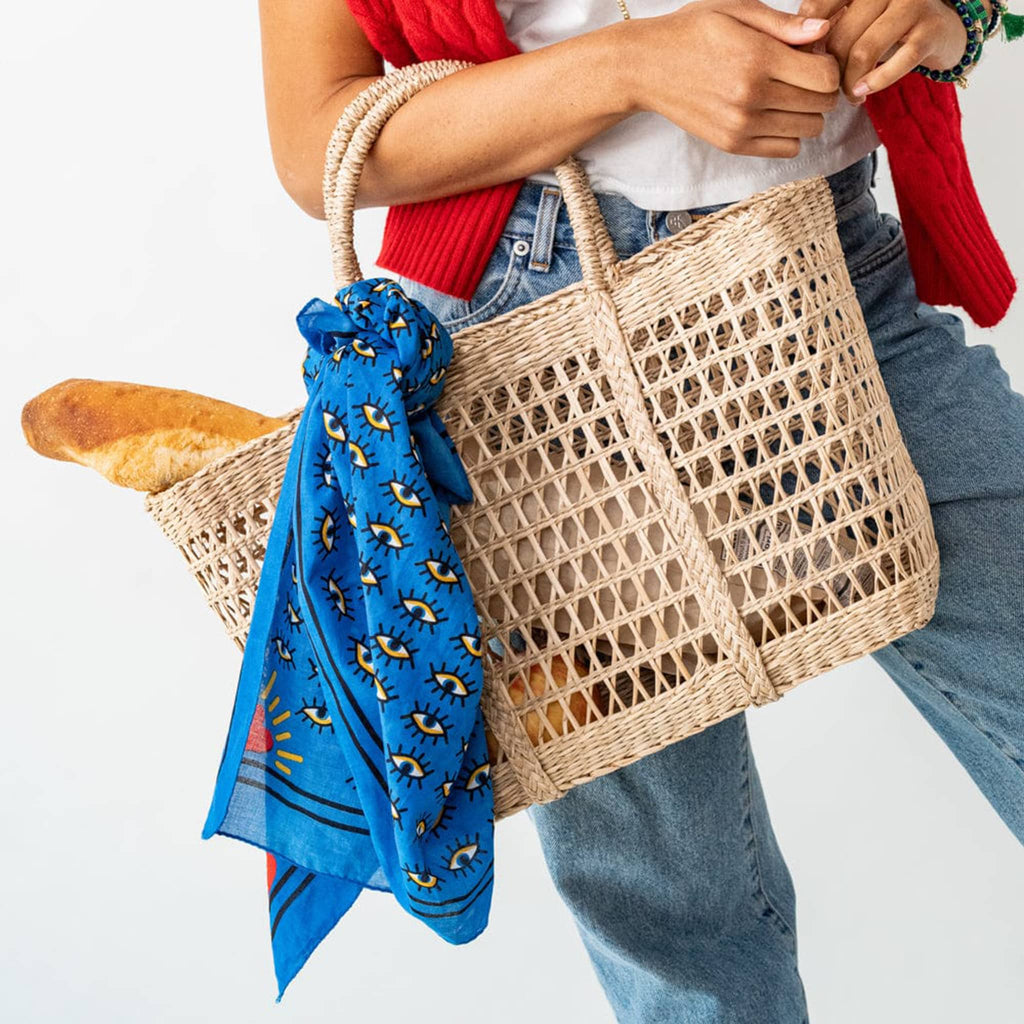Person holding a woven bag with a blue scarf and bread, with a red sweater and jeans.