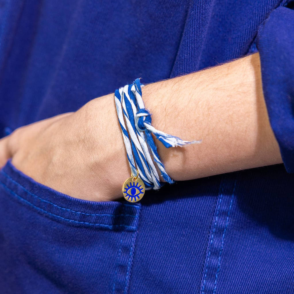 Person wearing a blue and white striped bracelet with a gold charm on a blue background.