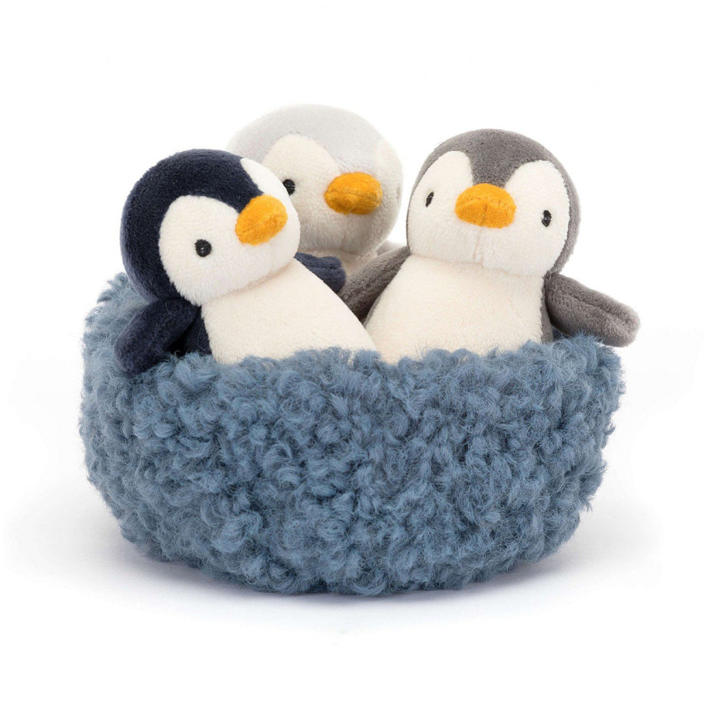 Jellycat Nesting Penguins, 3 little penguins in black, white and shades of gray in a furry blue nest, front view.