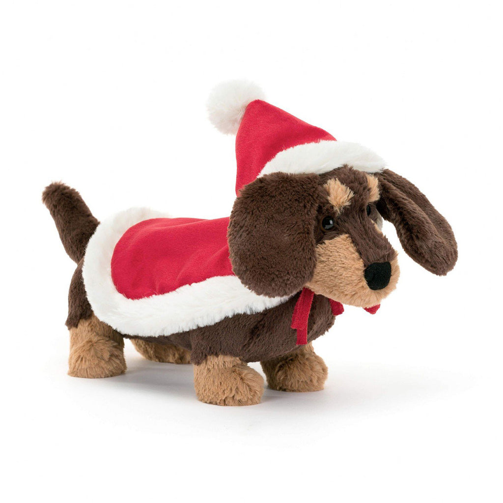 Jellycat Winter Warmer Otto Sausage Dog holiday plush toy, brown and tan sausage dog with a santa hat and matching red blanket with white furry trim on its back, front view.