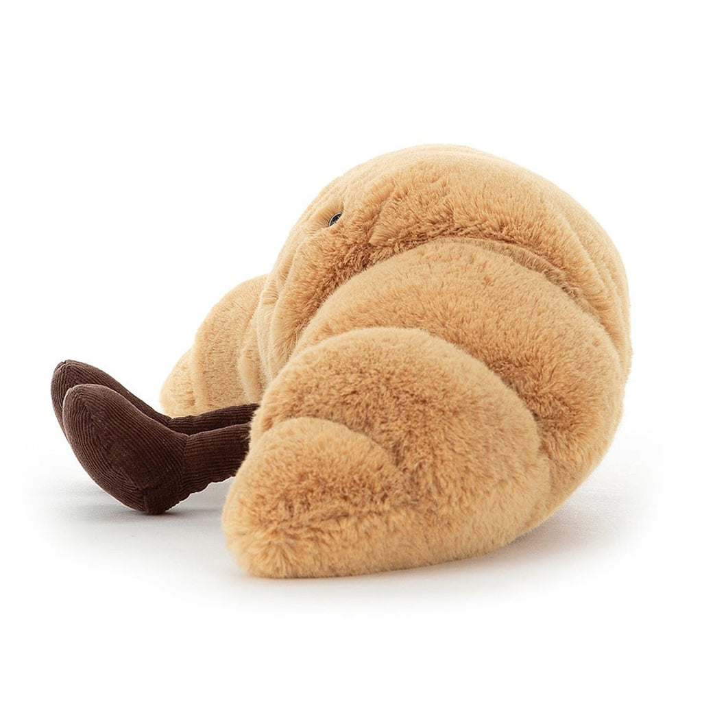 Jellycat small amuseable croissant plush toy, side view with brown corduroy feet, black bead eyes and a black stitched smile.