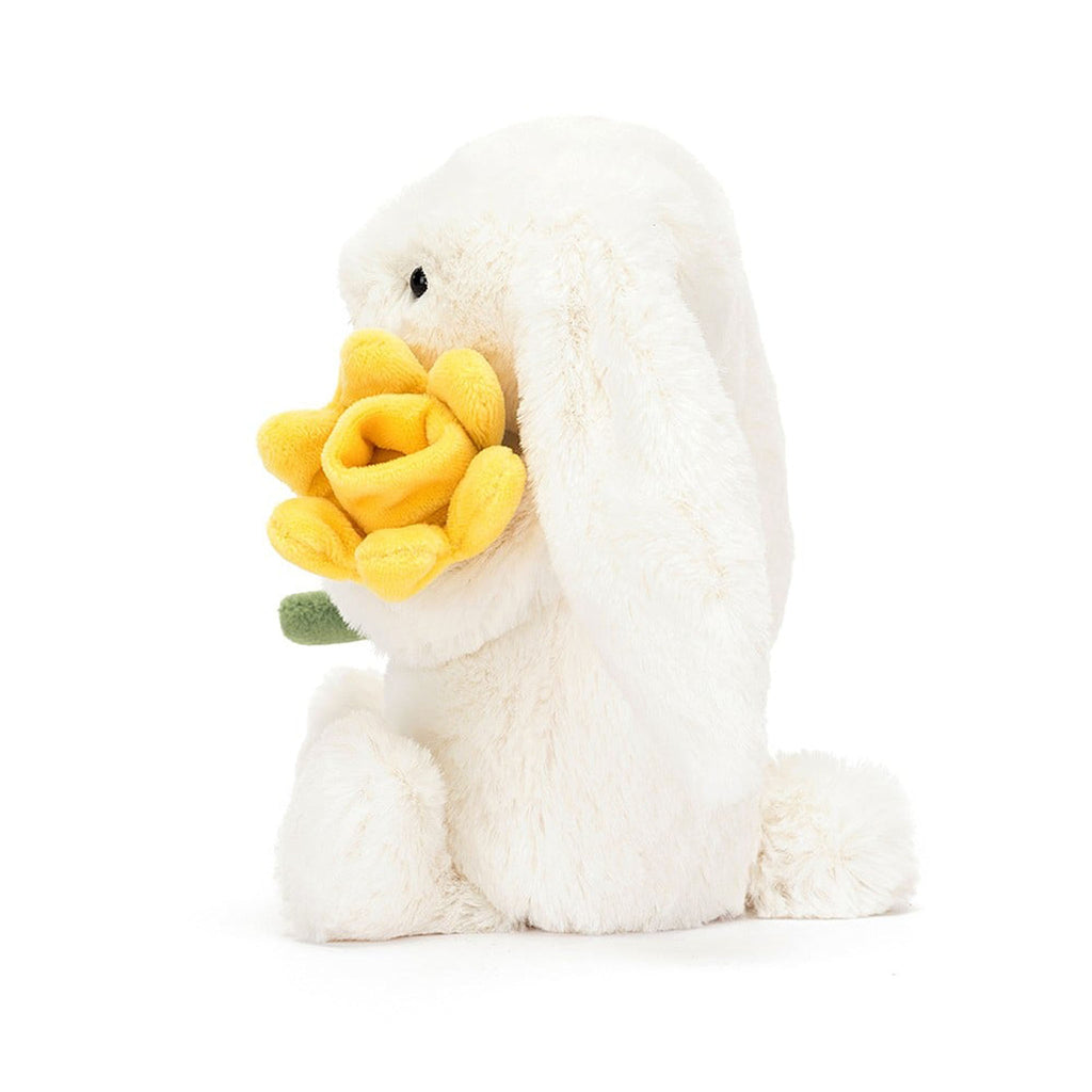 Jellycat cream bashful bunny holding a yellow daffodil plush toy, side view.