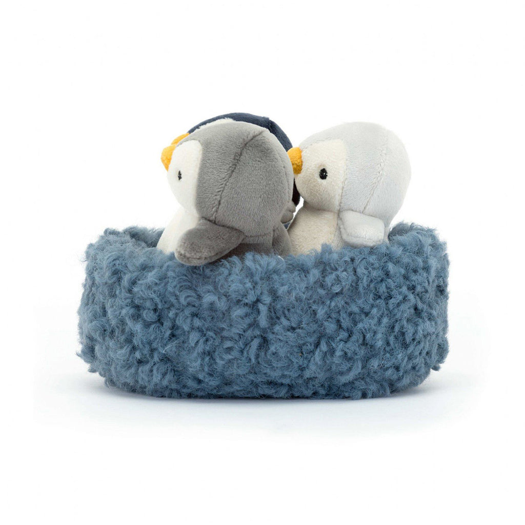 Jellycat Nesting Penguins, 3 little penguins in black, white and shades of gray in a furry blue nest, side view.