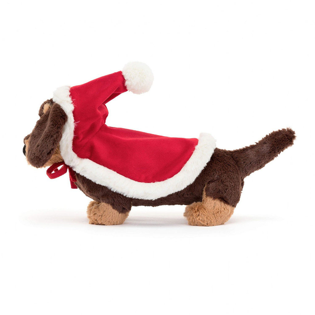 Jellycat Winter Warmer Otto Sausage Dog holiday plush toy, brown and tan sausage dog with a santa hat and matching red blanket with white furry trim on its back, side view.