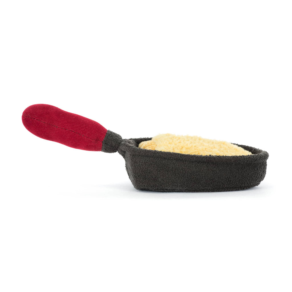 Plush brown raclette pan with smiling cheese inside and a red handle, back view on a white background.
