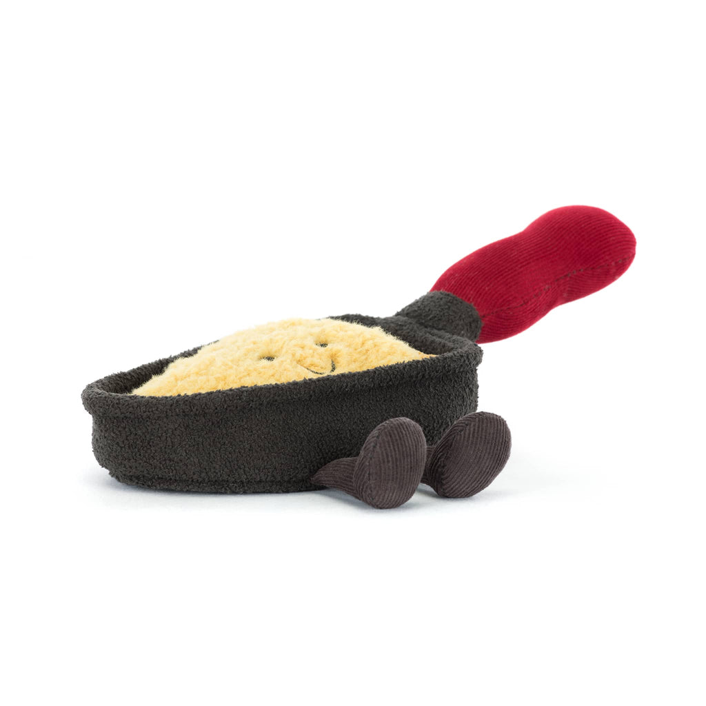 Plush brown raclette pan with smiling cheese inside and a red handle, front angle low view on a white background.