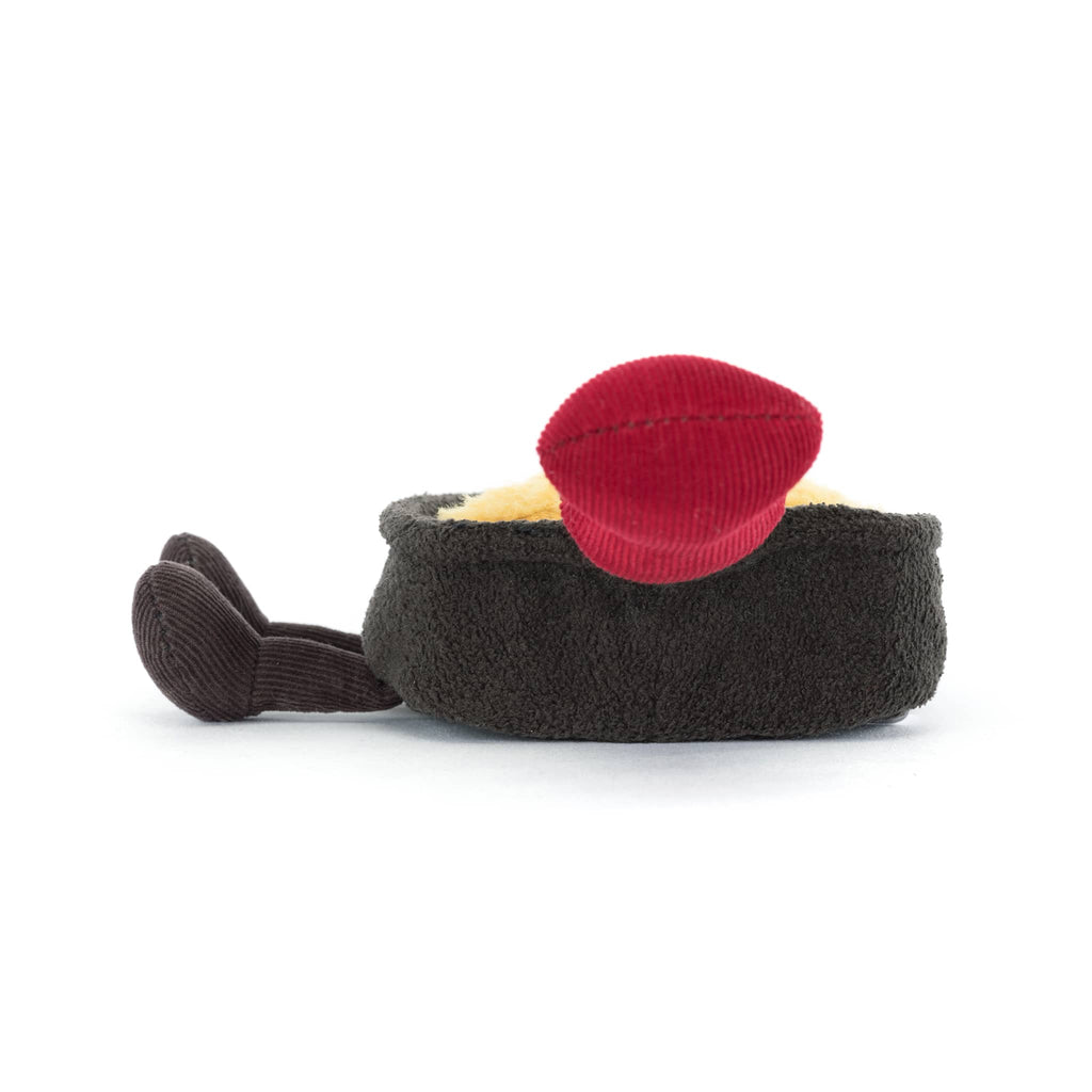 Plush brown raclette pan with smiling cheese inside and a red handle, side view on a white background.