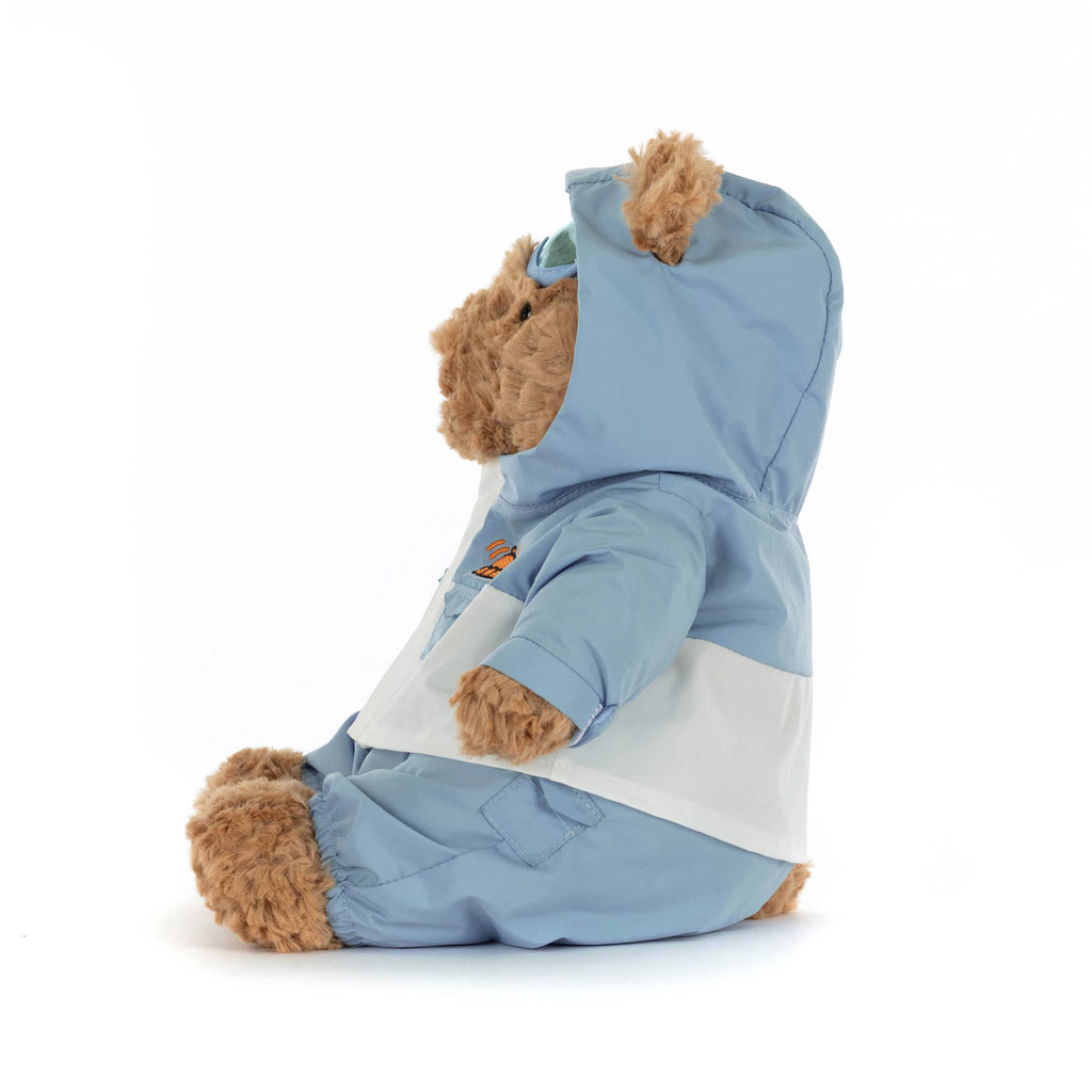 Plush teddy bear wearing a blue and white snowsuit, side view on a white background.