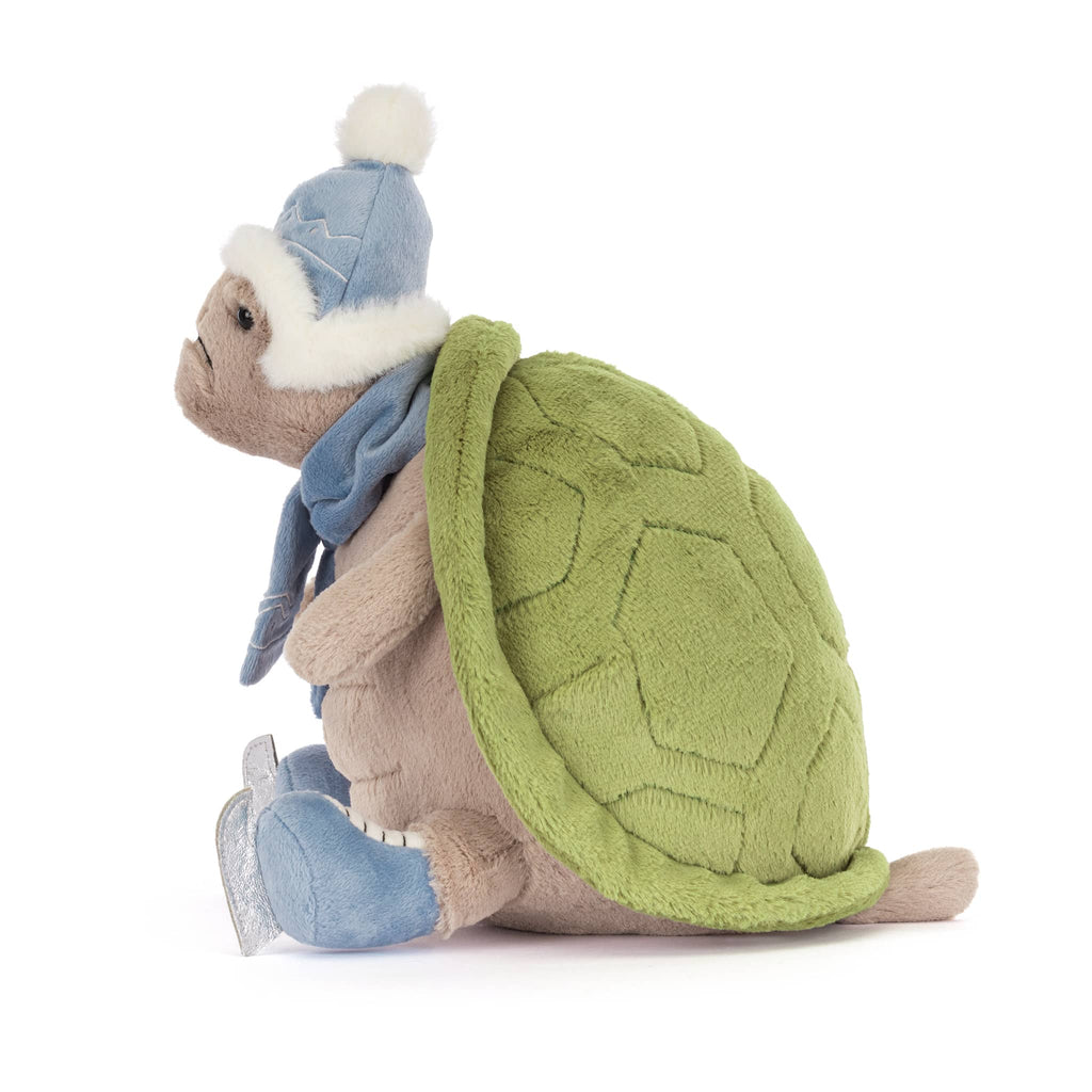 Plush turtle wearing a blue winter hat, scarf, and ice skates, side view on a white background.