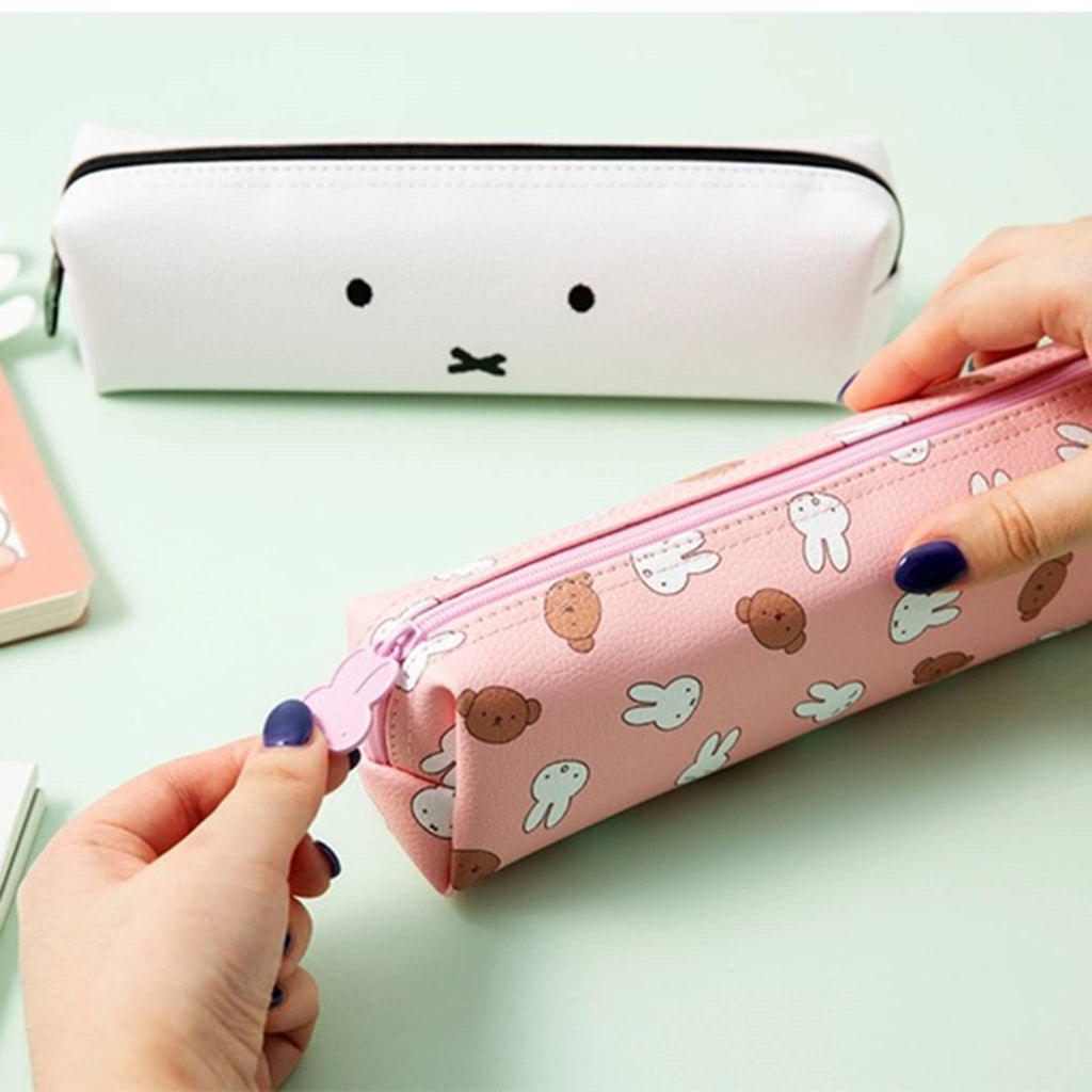 Pink pencil case with cartoon designs held by a hand with white pencil case with face, on a light green background.