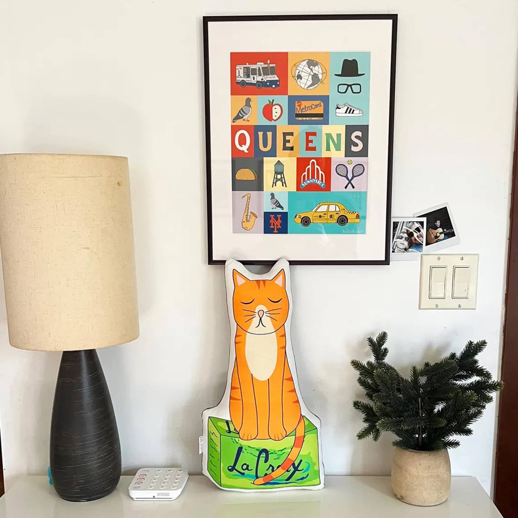 Bodega cat-shaped pillow on a white table  against a wall in a room setting.