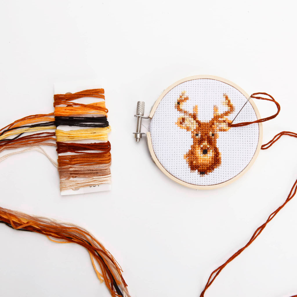 Embroidery hoop with a deer design and cross-stitching thread on a white background.