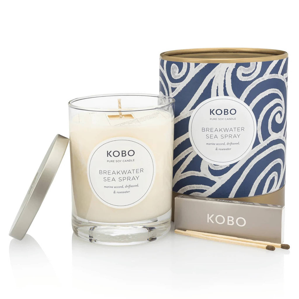 KOBO 11 ounce Breakwater Sea Spray candle, part of the Coastal Collection, in clear glass vessel with metal lid next to blue and white wave illustrated canister packaging with a pack of wooden matches.