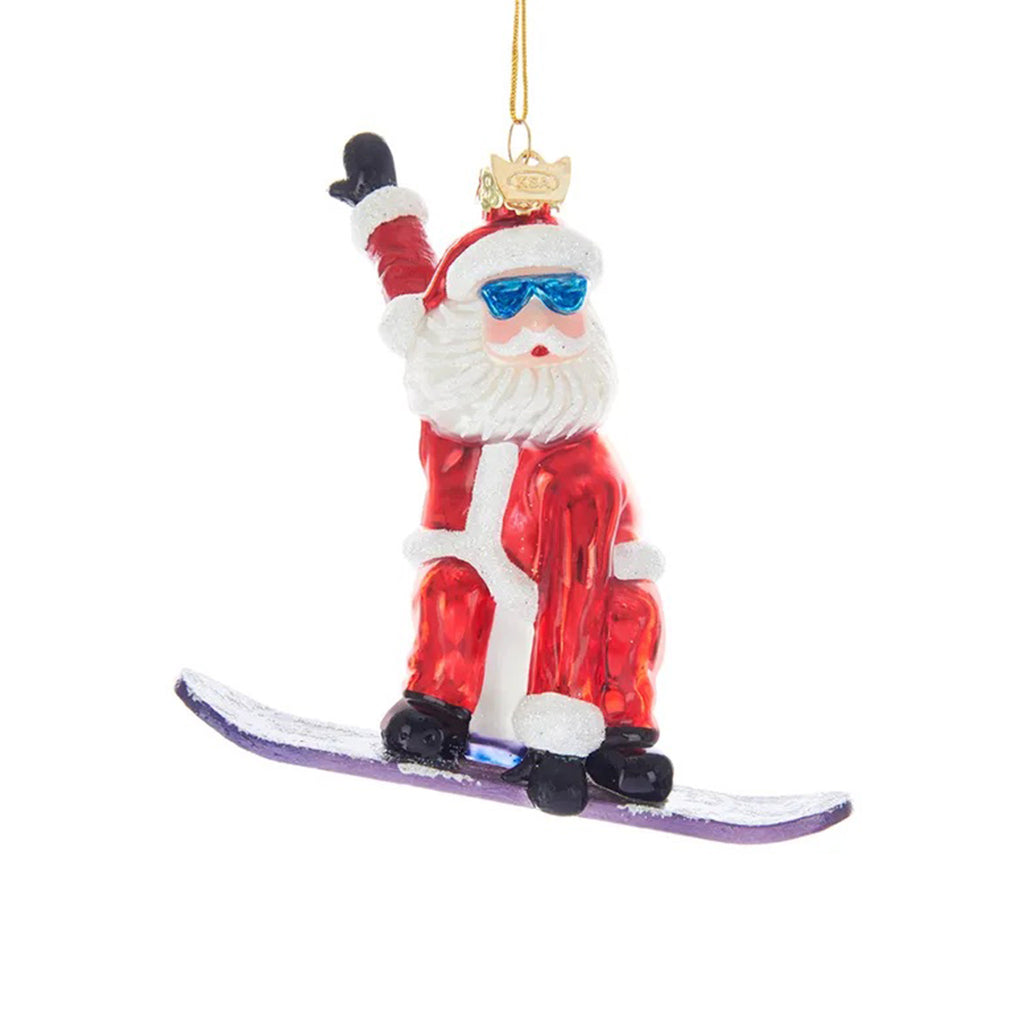 Kurt Adler Noble Gems Collection Santa Claus in traditional suit riding a purple snowboard hanging glass holiday tree ornament.