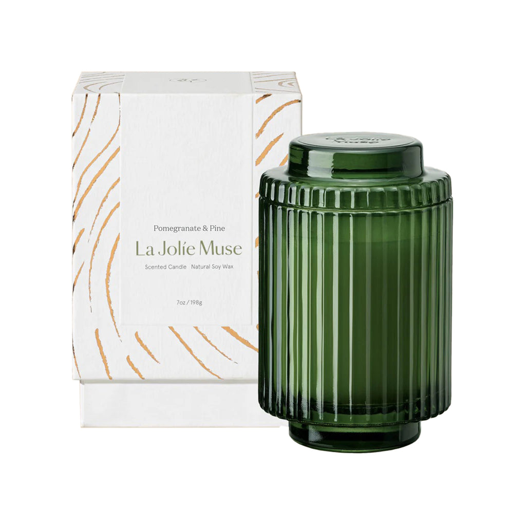 La Jolie Muse Amelie 7 ounce Pomegranate and Pine scented soy wax candle in ribbed green glass vessel with lid, in front of white gift box.