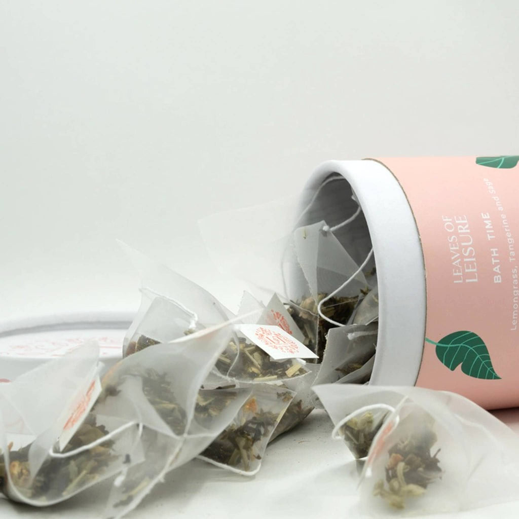 Leaves of Leisure Bath Time Lemongrass, Tangerine and Sage Low Caffeine Organic Tea in illustrated peach canister packaging, lid off with tea bags spilling out.
