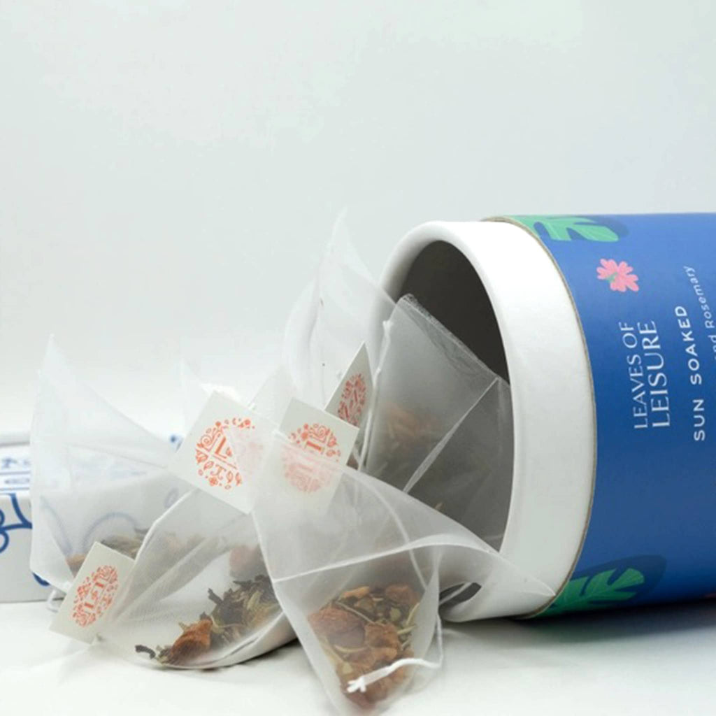 Leaves of Leisure Sun Soaked Low-Caffeine Organic Tea in illustrated blue canister packaging, lid off with tea bags spilling out.