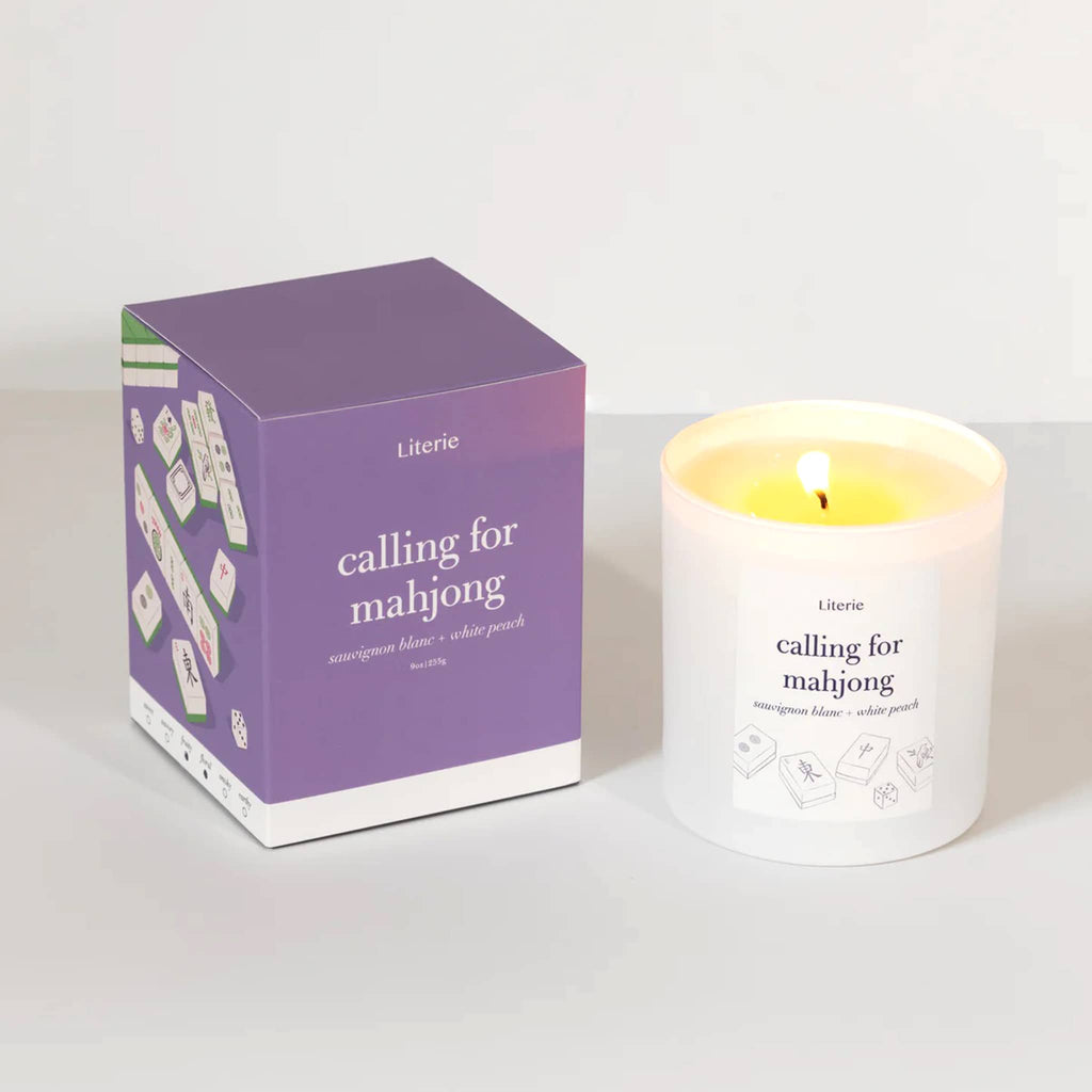 Literie Calling for Mahjong sauvignon blanc and peach scented candle in matte white vessel, wick lit, with purple gift box.