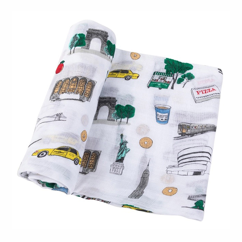 Little Hometown NYC Baby Swaddle Blanket made from a bamboo and cotton blend muslin with illustrations of NYC icons on a white background, partially unrolled to show print.