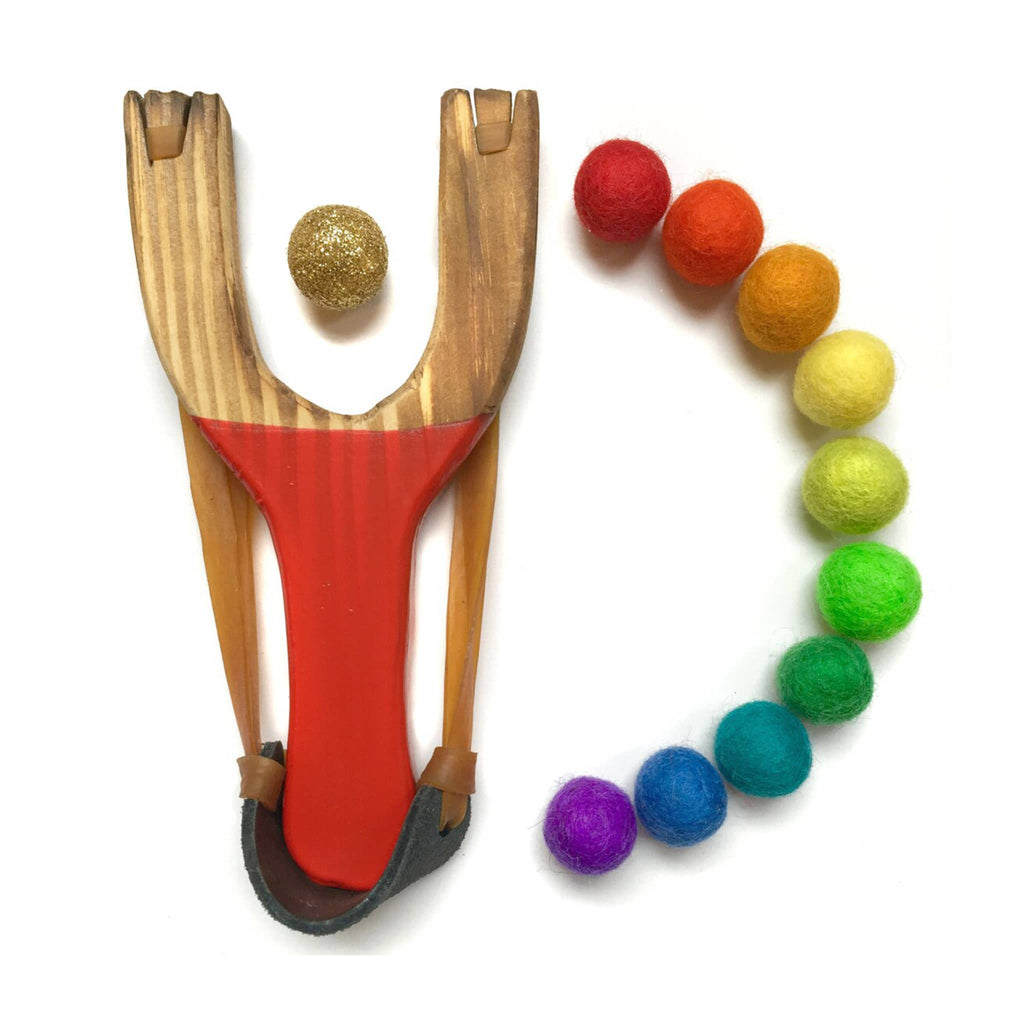 Little Lark Kids Deluxe wooden slingshot with red handle and 1 gold glitter felt ball and 10 felt balls in rainbow colors.