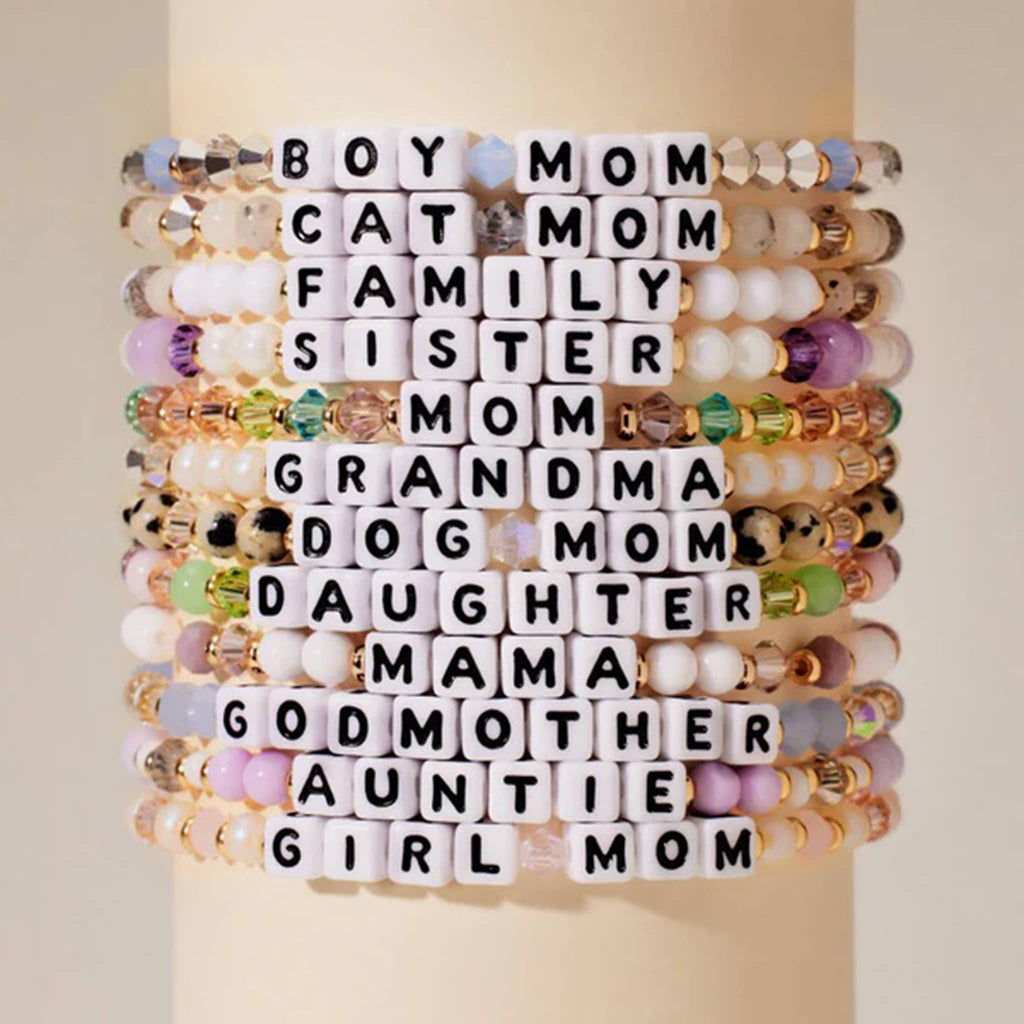 Little Words Project Grandma beaded elastic bracelet in strand of pearls bead design, faux cream pearls with white and gray translucent faux crystal beads, gold spacer beads and letter beads. Shown in a stack with similar bracelets.