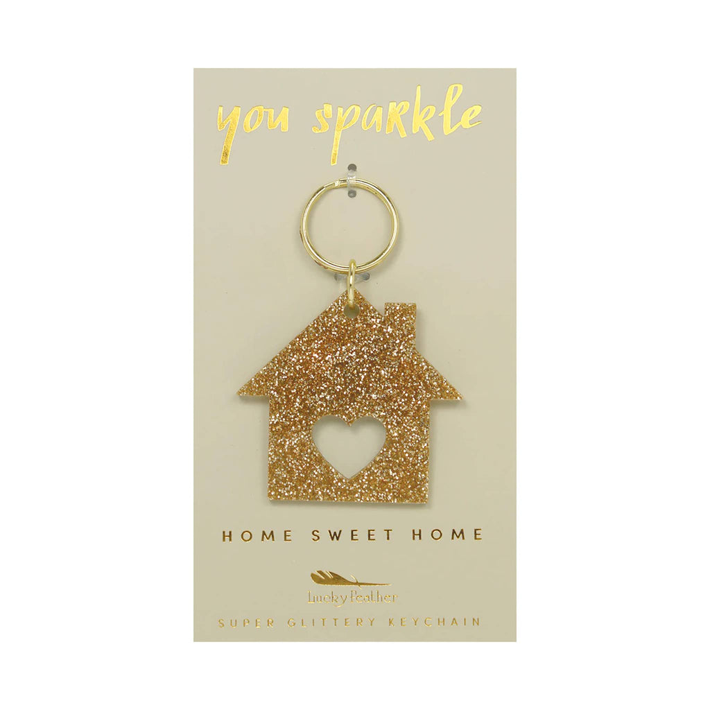 Gold glitter house-shaped keychain on a beige card with 'you sparkle' and 'home sweet home' text.